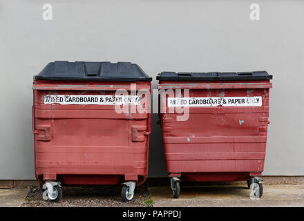 Two red coded commercial bins in front of a light grey wall Stock Photo