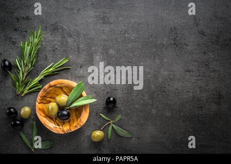 Black and green olives and oil  in wooden bowl on black slate background. Top view  with space for text. Stock Photo