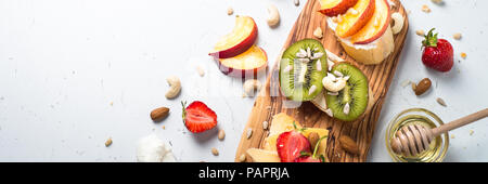 Fresh sweet fruit sandwiches. Strawberry peach and kiwi sandwiches with nuts and honey over white table. Healthy snack. Long banner web format. Stock Photo