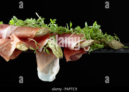 Asparagus wrapped in prosciutto with cress salad on a black background. Copy space for your text. Stock Photo