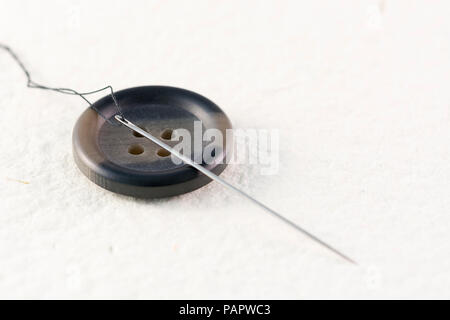 Close up of a button with needle and thread on a white background Stock Photo