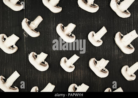 White sliced mushrooms on black wood rustic background, top view. Flat lay pattern of white champignons on table Stock Photo