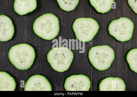 Fresh sliced cucumbers on black wood rustic background, top view. Flat lay pattern of green cucumbers on table, close-up Stock Photo