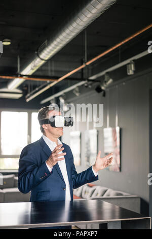 Mature businessman wearing VR glasses holding snowboard in office with ...