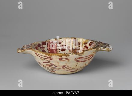 Scudello. Culture: Spanish, Valencia. Dimensions: Width across handles: 7 in. (17.8 cm). Date: 16th century.  Tin-glazed earthenware, of which lusterware is one type, was developed in the Middle East in the ninth and tenth centuries to imitate the porcelains produced in China. The opaque white glaze concealed the clay body, which could range from pale buff to brick red, allowing for brilliant effects created by painting the white surface with metal oxides that fired to a range of colors. This technique, as well as the use of metallic luster--an iridescent, coppery painted glaze--spread through Stock Photo