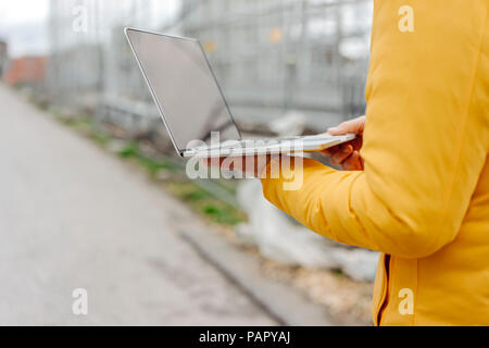 Man holding laptop, construction site in the background
