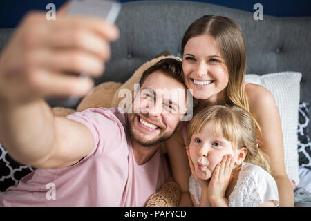 Happy family sitting on bed, taking smartphone selfies Stock Photo