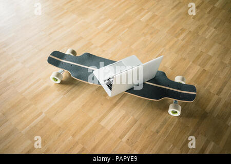 Laptop and longboard on wooden floor Stock Photo