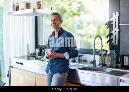 Smiling mature man at home in kitchen with cup of coffee Stock Photo
