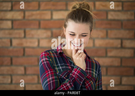 Portrait of hesitating young woman in front of brick wall Stock Photo