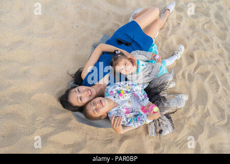 Happy mother with two daughters lying on the beach Stock Photo