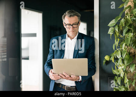 Mature businessman standing in office using laptop Stock Photo