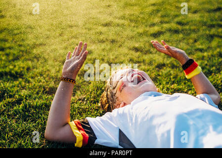 Boy in German soccer shirt lying on grass, laughing and screaming Stock Photo