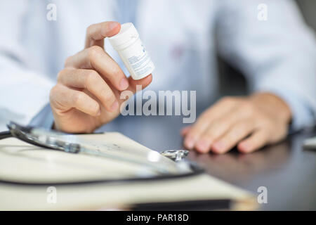 Doctor sitting at his desk holding pills Stock Photo