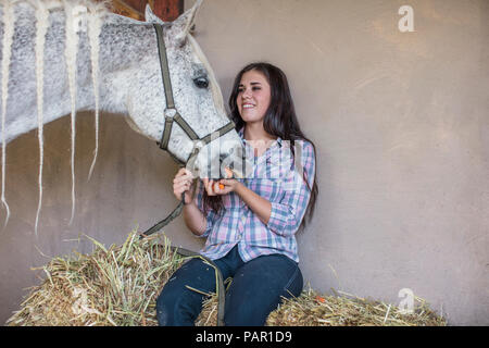 Smiling woman feeding a horse on a farm Stock Photo