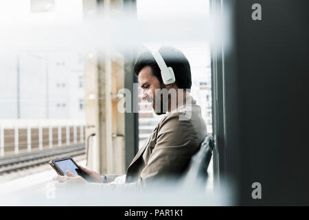 Smiling young man wearing headphones using tablet at the station platform Stock Photo