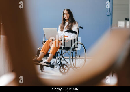 Young handicapped woman sitting in wheelchair, using laptop Stock Photo