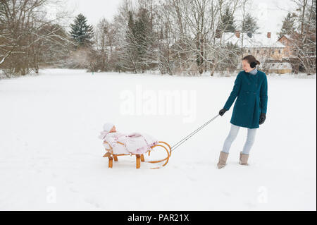 Mother pulling little daughter on sledge Stock Photo