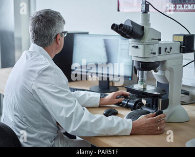 Physician working with microscope, looking on screen Stock Photo