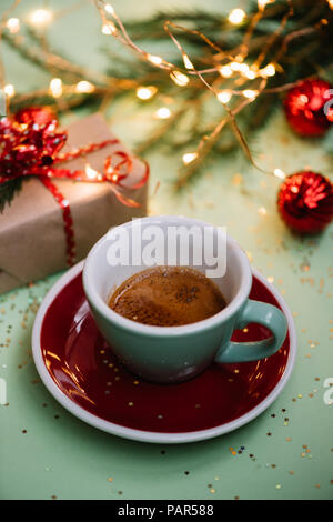 Delicious fresh morning winter festive espresso coffee in a green mug and a red saucer on the green background with christmas decoration, girts wrappe Stock Photo