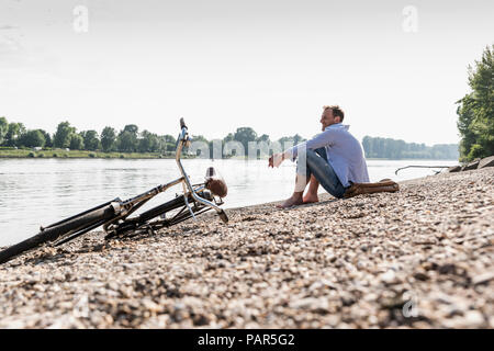 Mature man with bike sitting at Rhine riverbank Stock Photo