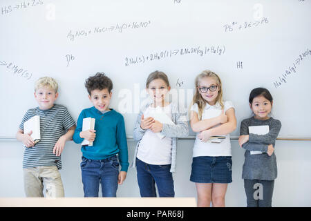 Portrait of smiling pupils standing at whiteboard with formulas in class Stock Photo