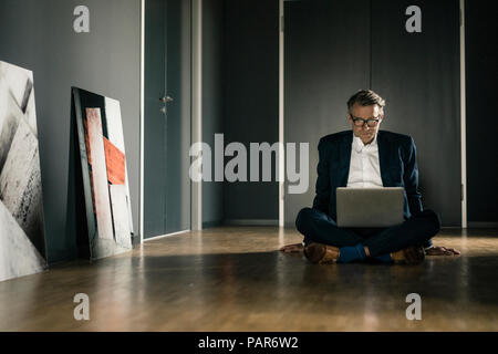 Mature businessman using laptop on office floor Stock Photo