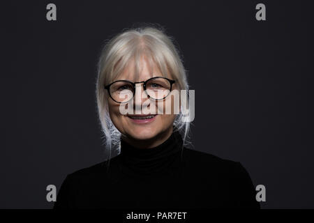 Portrait of smiling senior woman wearing glasses in front of dark background Stock Photo