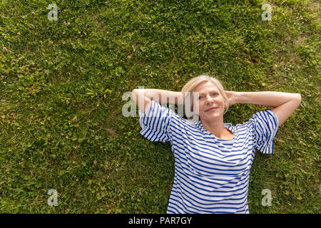 Portrait of smiling senior woman lying in grass Stock Photo