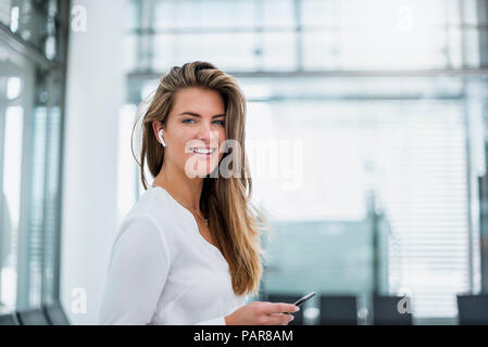 Smiling young woman wearing in-ear phone using cell phone Stock Photo