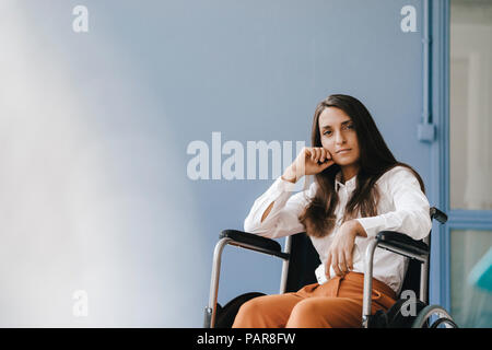 Young handicapped woman sitting in wheelchair, looking worried Stock Photo