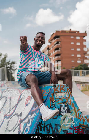 Young man in skatepark sitting on wall, laughing Stock Photo