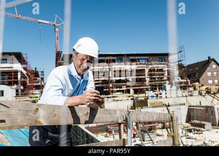 Man wearing hard hat using cell phone on construction site Stock Photo