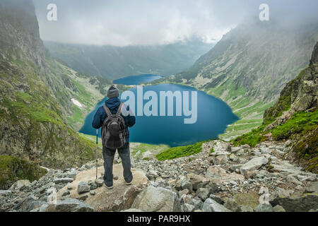 A man with trekking poles and backpack staying and looking at Czarny Staw pod Rysami and Morskie Oko lakes in Tatra Mountains Stock Photo
