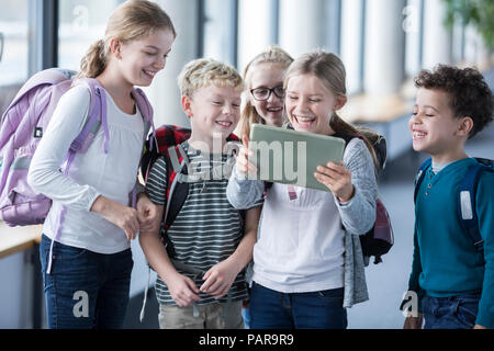 Laughing pupils looking at tablet on school corridor Stock Photo