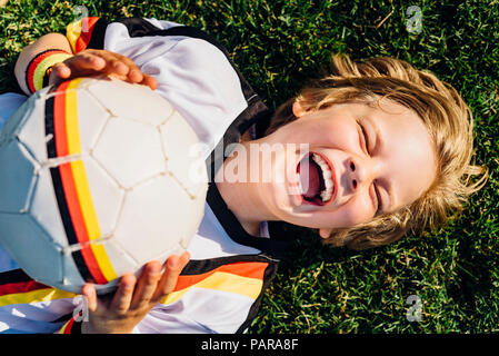Boy in German soccer shirt lying on grass, laughing happily Stock Photo