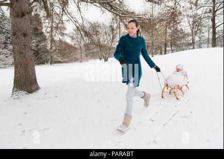 Mother pulling little daughter on sledge Stock Photo