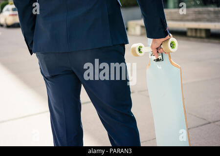 Businessman holding longboard outdoors Stock Photo