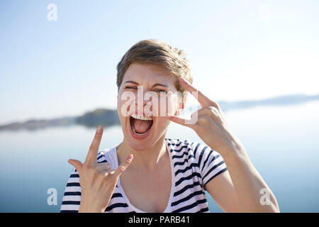 Portrait of screaming woman in front of lake showing Rock And Roll Sign Stock Photo