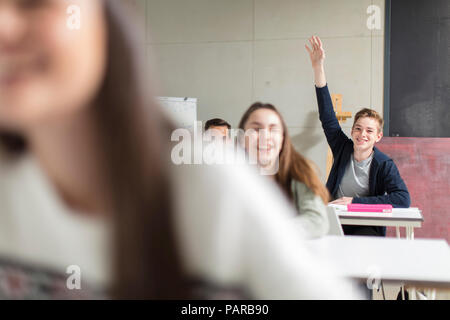 Smiling teenage boy raising hand in class Stock Photo