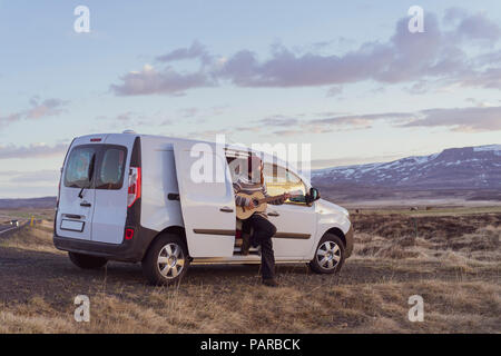 Iceland, young man leaning on van and playing guitar Stock Photo