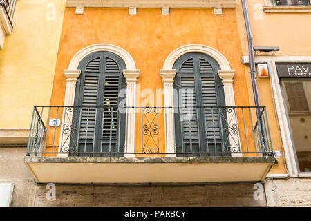 bright yellow mustard, italian balcony, with double windows, and closed wooden shutters, verandah, verona Italy Stock Photo