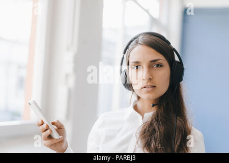 Young woman using smartphone, wearing headset Stock Photo