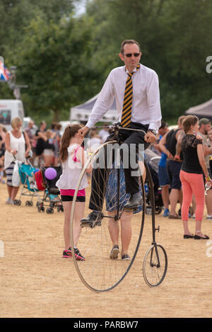 Man riding a penny-farthing bicycle at a family festival in summer. Stock Photo