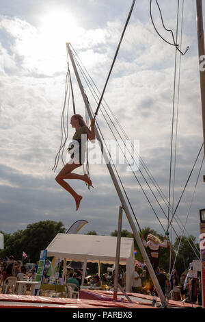 Teenage girl on a bungee trampoline at a family festival in summer silhouetted by the sun. Stock Photo