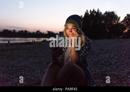 Young woman using smartphone on riverside in the evening Stock Photo