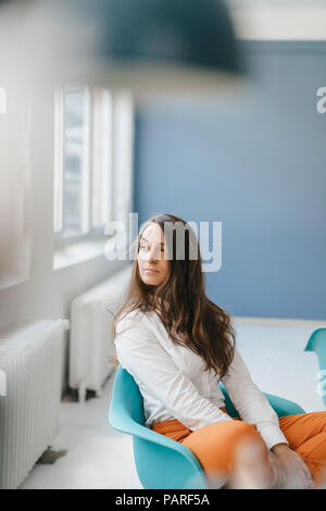 Young woman sitting in chair, looking out of window Stock Photo