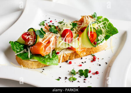 Bruschetta with salmon red fish, fresh vegetables and herbs on a white plate Stock Photo