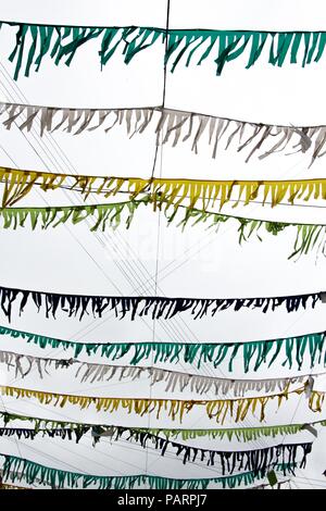 Small multicolored flags are attached to the thread and hang against the background of the sky that has been clouded. They cringe from a strong vertic Stock Photo