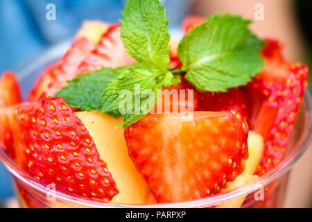 Fresh and fragrant sliced berries and fruits are stacked in a container. Yellow melon and red strawberry. Everything is decorated with a fragrant bran Stock Photo